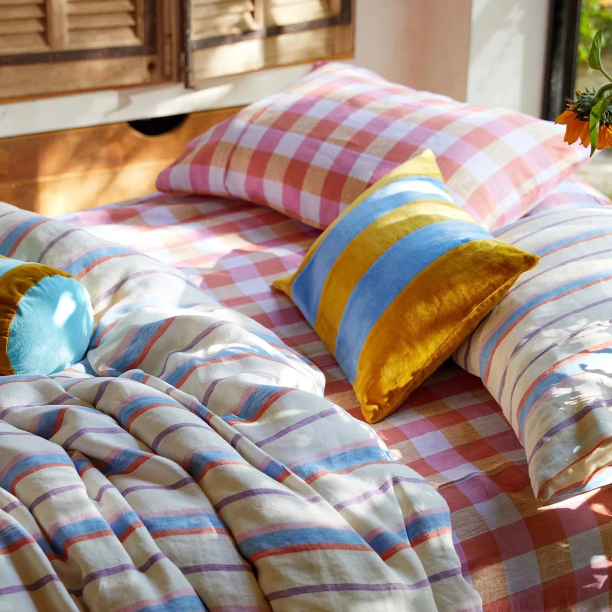Bed styled with stripe quilt cover and summer check fitted sheet and matching standard pillowcases. Decorative pillow with mustard and blue stripes. 
