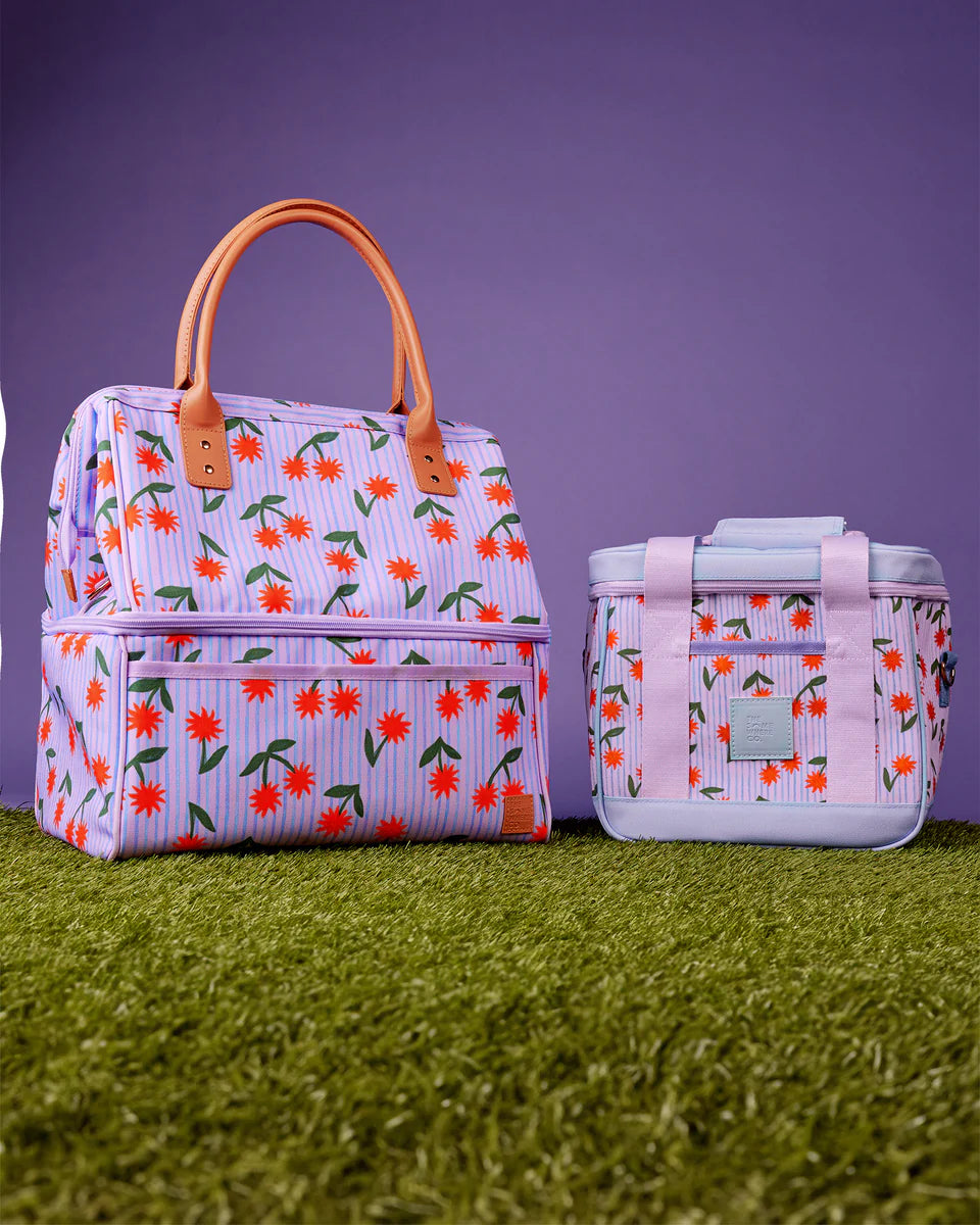 Floral-patterned insulated lunch bag and cooler on grass with purple background
