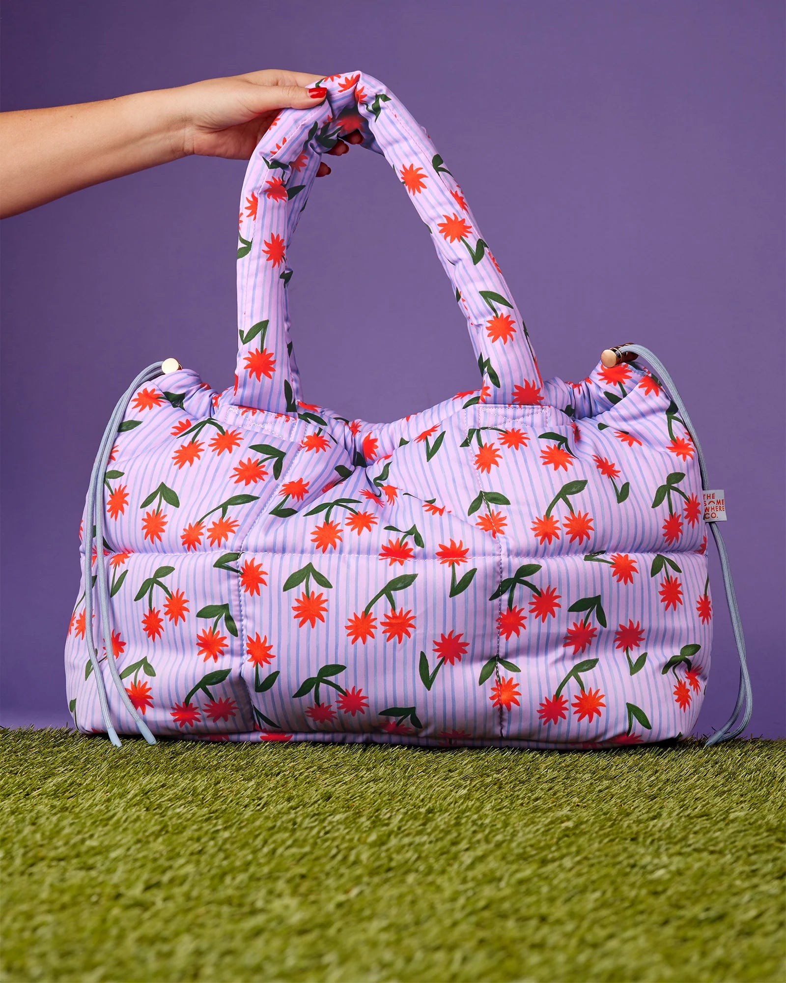 Floral patterned bag held by a hand on a purple and green background