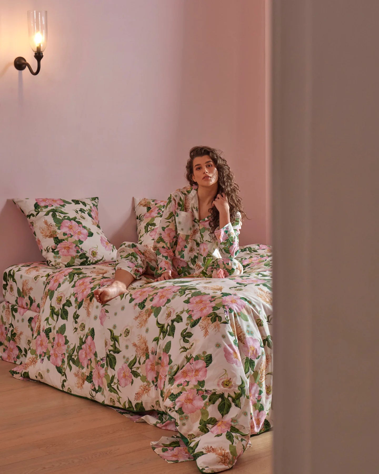 Woman sits on top of bed in matching pyjamas to quilt cover and pillowcases all in Sunday Stroll cotton print. 