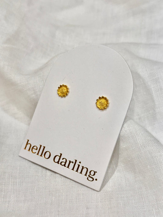 Gold earrings on a 'hello darling' card against a white fabric background