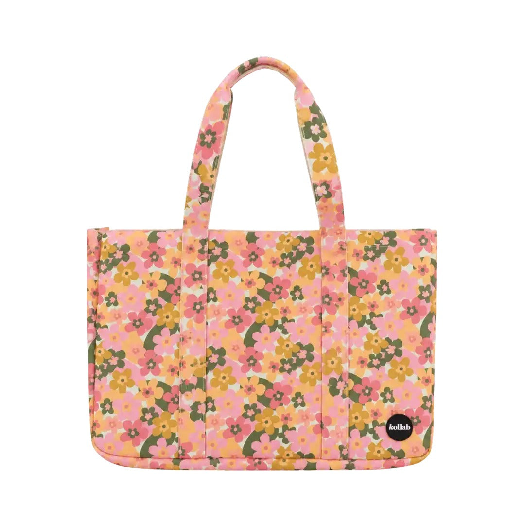 A pink floral tote bag with yellow, green, and orange flowers, featuring two top handles and a small black circular 'kalliope' logo patch on the bottom right, set against a plain white background.