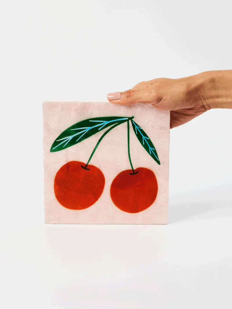 Hand holding a pink napkin with red cherries and green leaves on a white background