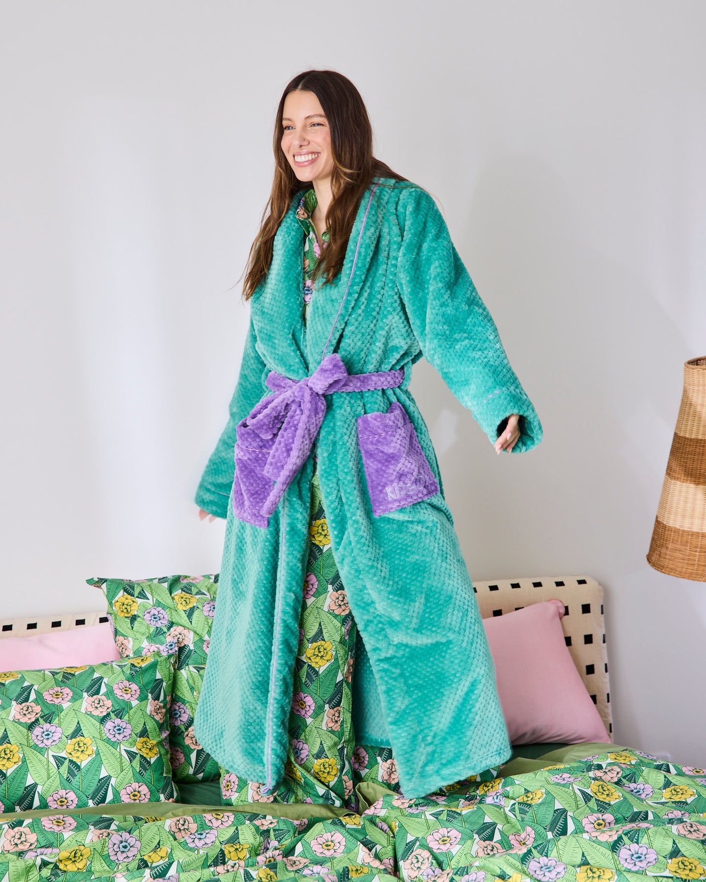 Woman wearing a teal robe with purple accents in a bedroom setting