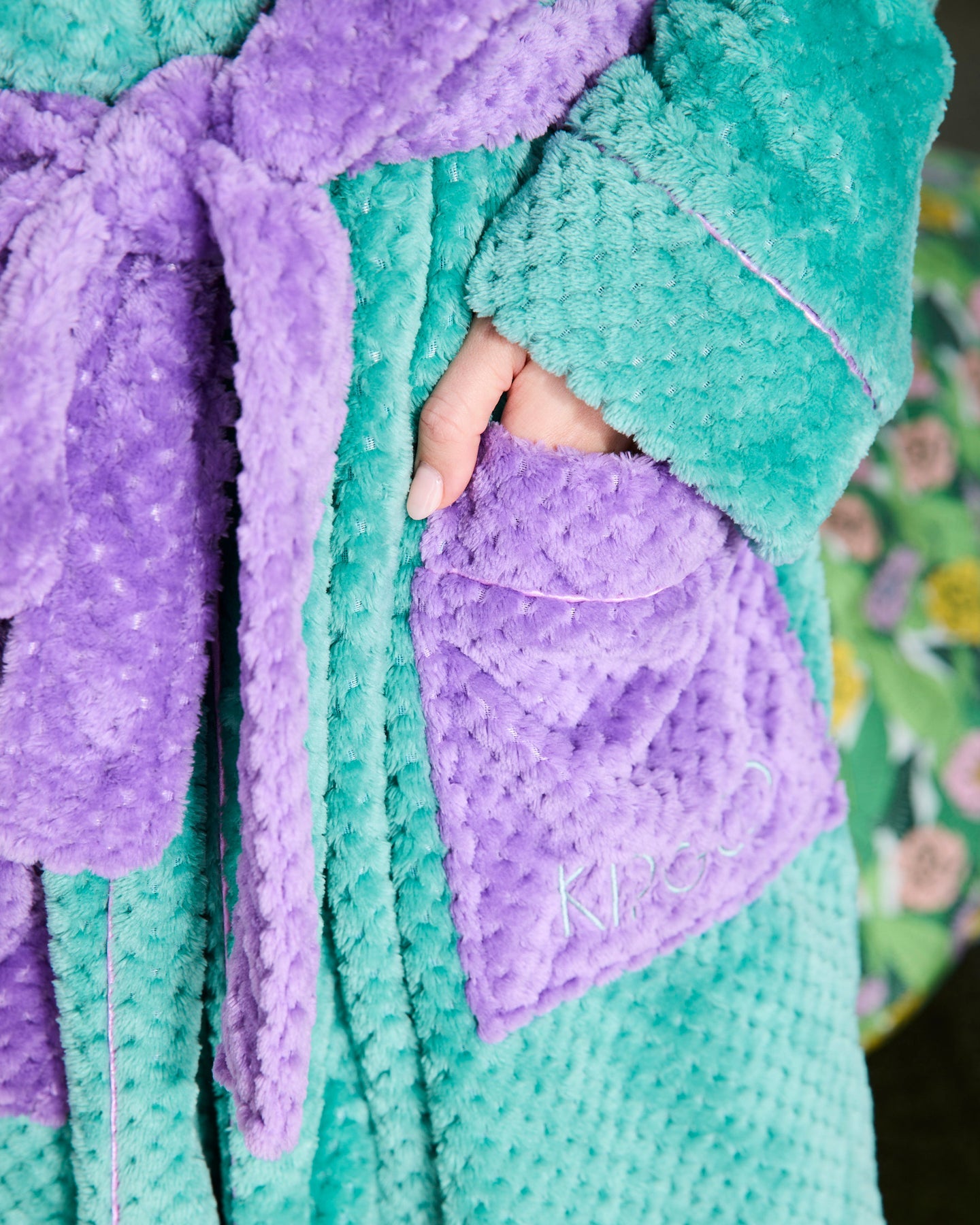 Close-up of a teal and purple robe with a brand logo on a floral background