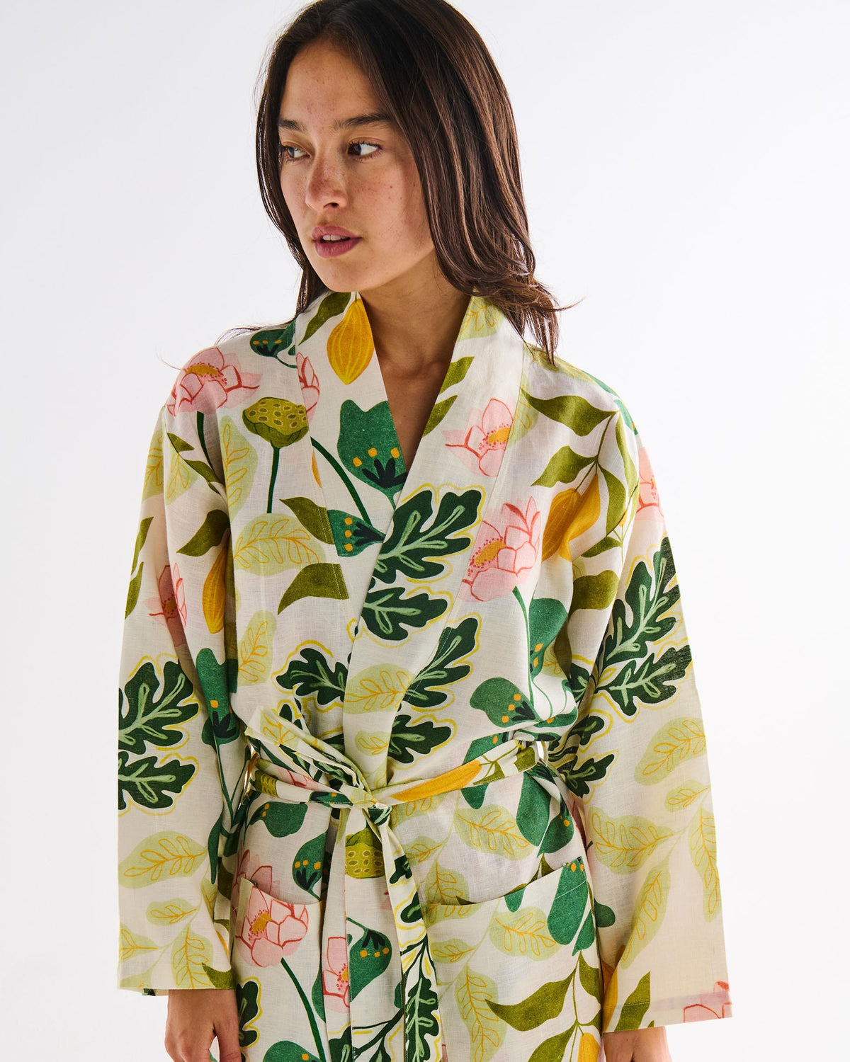 A woman wearing a cream-colored wrap robe with a vibrant green, yellow, and pink botanical leaf pattern, photographed against a clean white background.