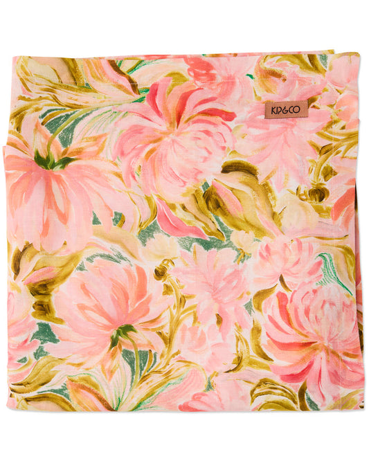 A folded square scarf featuring a vibrant watercolor floral print in shades of pink, peach, olive green, and cream, with a small brown leather brand tag reading 'KO6CO' on the upper right.
