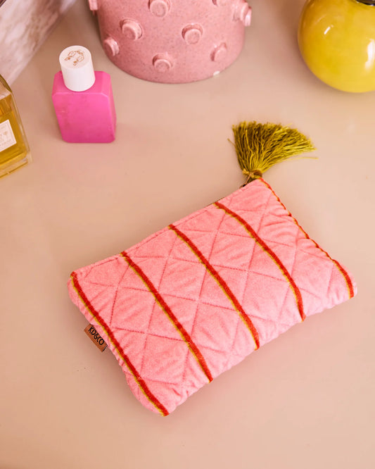 Pink pouch with yellow stripes and tassel on a beige surface with decorative items.