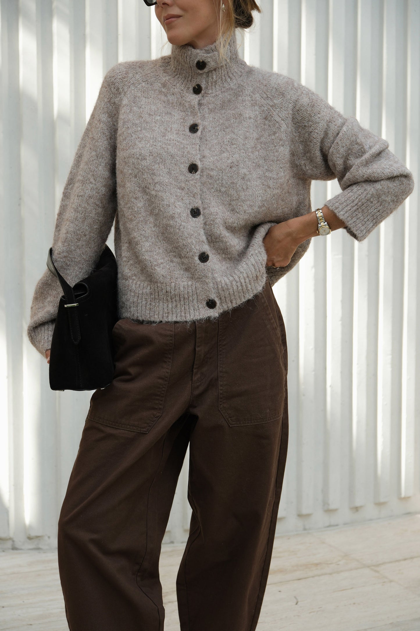 Person wearing a gray button-up sweater and brown pants with a black bag.