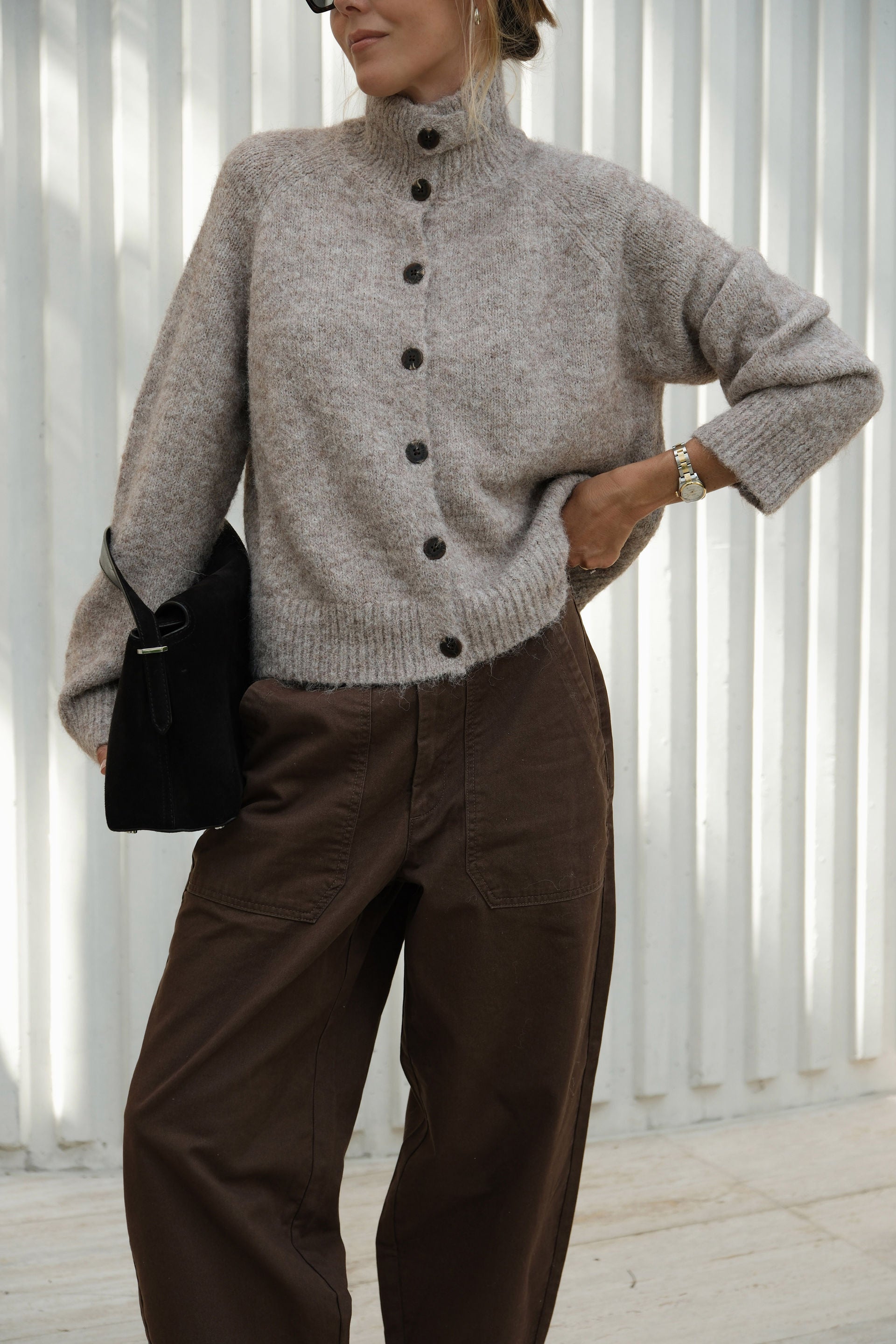 Person wearing a gray button-up sweater and brown pants with a black bag.