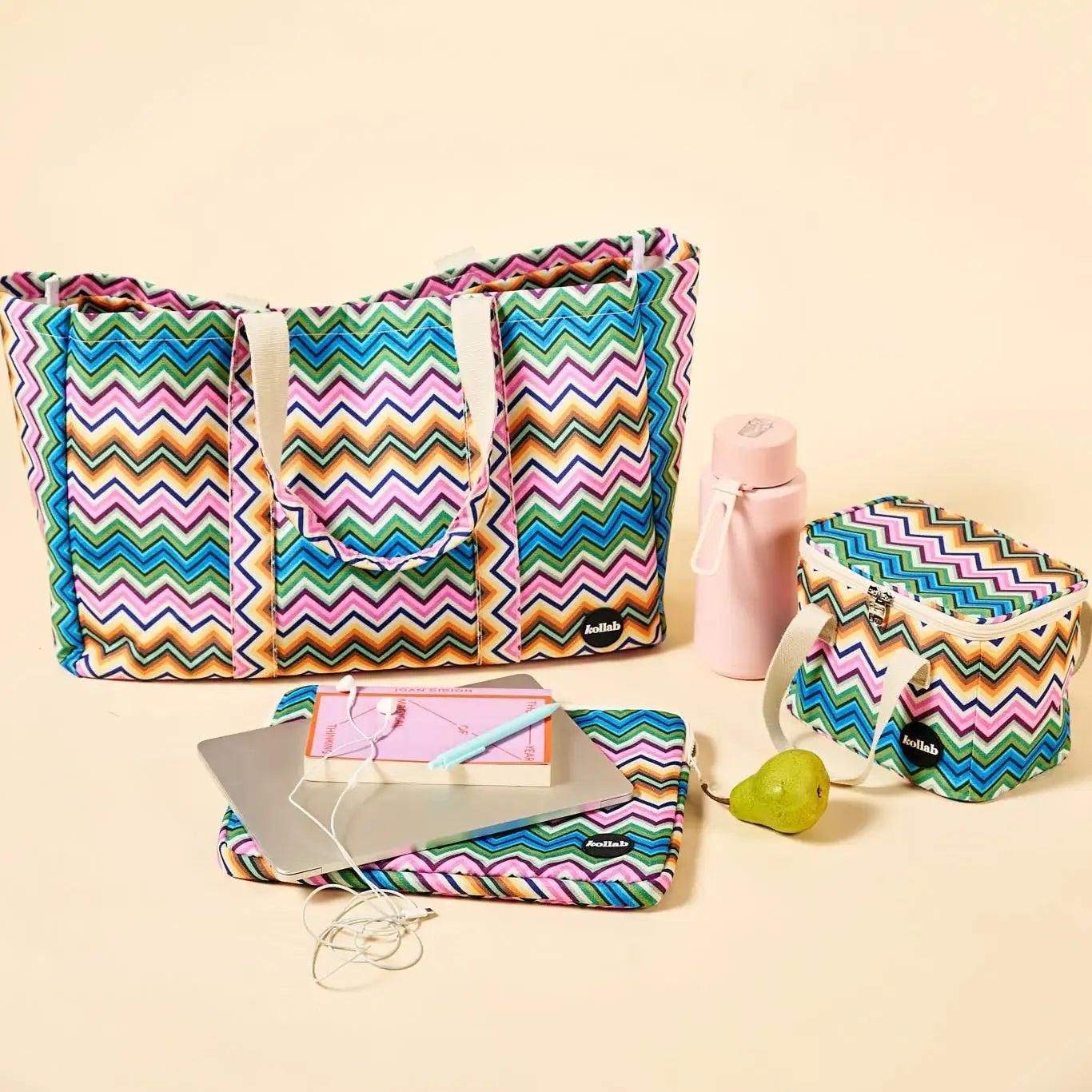 A coordinated set of colorful zigzag-patterned bags and accessories arranged on a warm cream background. The set includes a large tote bag, a laptop sleeve, a small pouch, a pink water bottle, and a small green pear-shaped accessory.